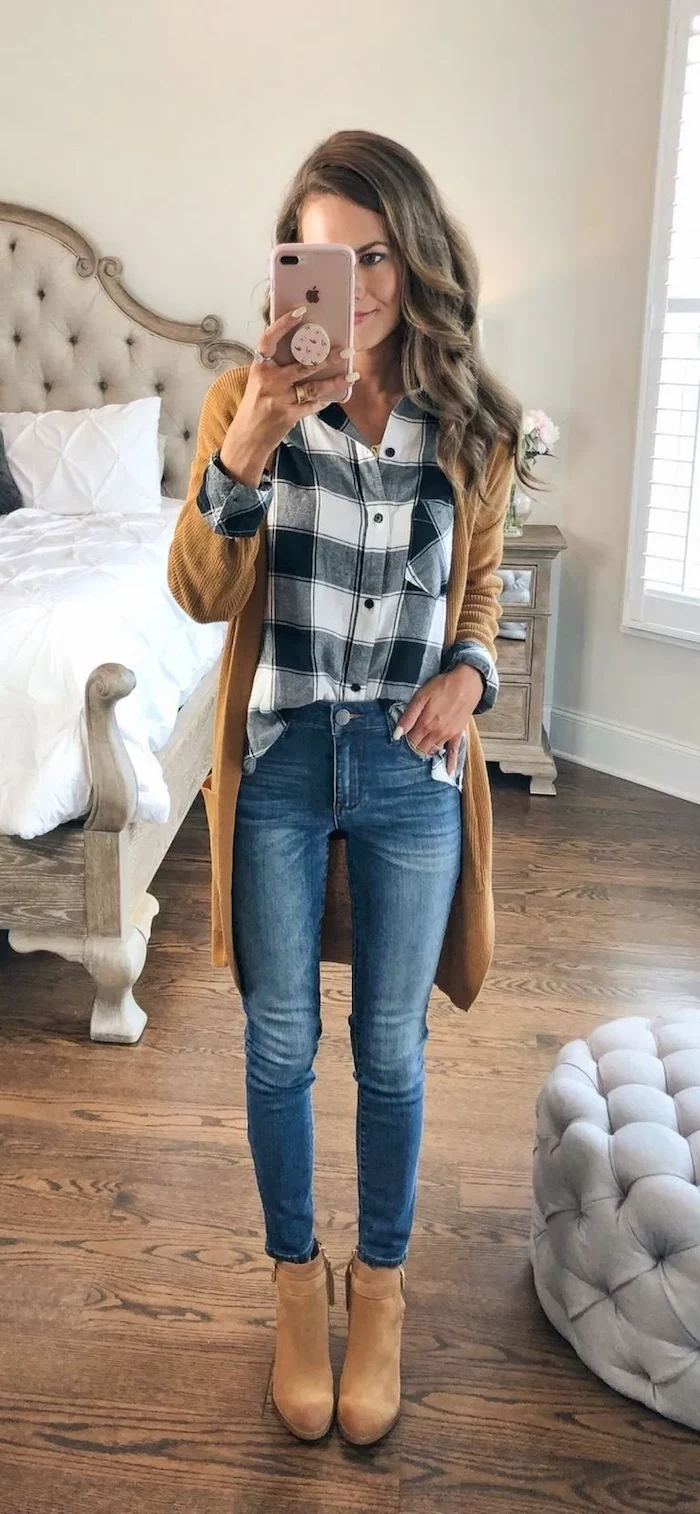 cute outfit ideas woman with light brown wavy hair taking a selfie in the mirror wearing jeans plaid shirt brown velvet boots brown cardigan