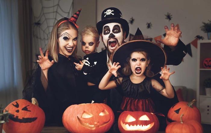 dad mom and two kids dressed in scary costumes making scary faces family of 3 halloween costumes jack o lanterns in front of them