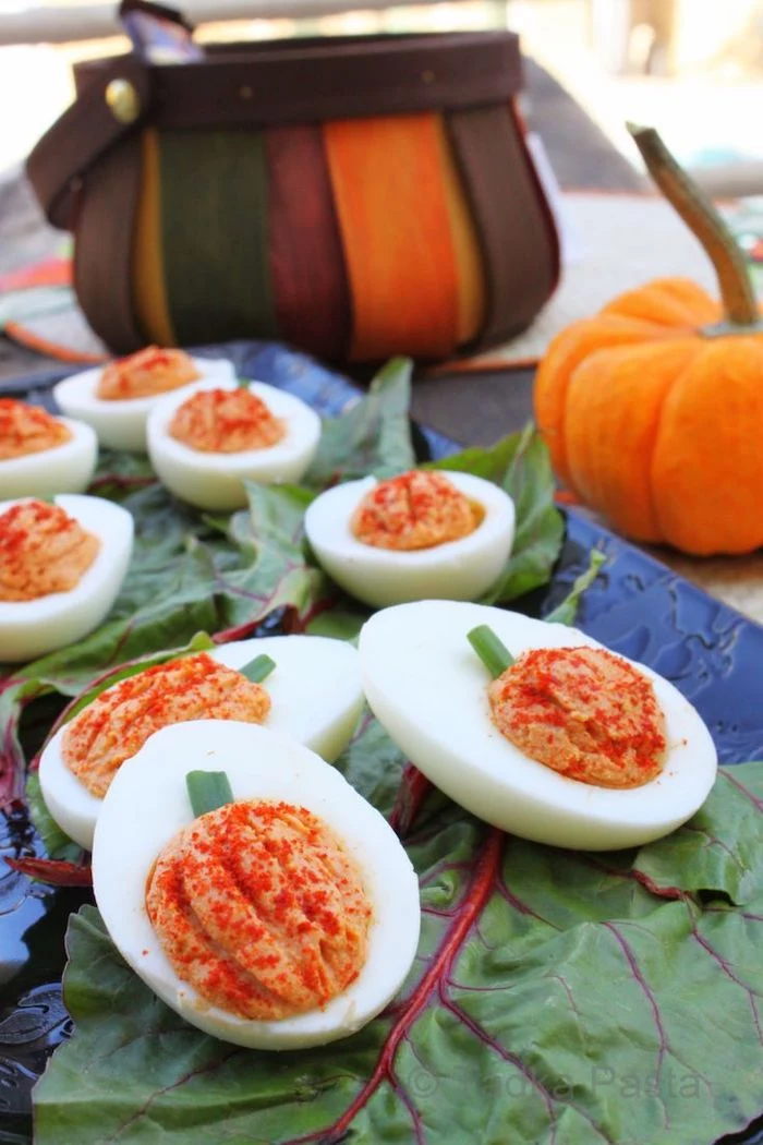 deviled eggs with filling made in the shape of pumpkin halloween party snacks arranged on green leaves on blue tray