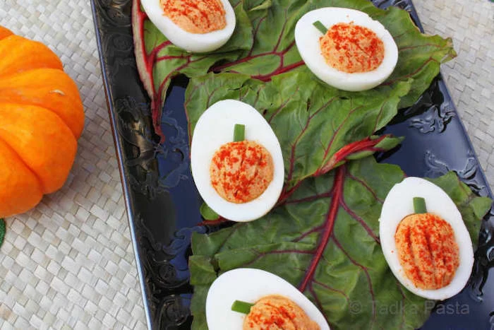 deviled eggs with filling made in the shape of pumpkins placed on green leaves on blue tray halloween appetizer ideas