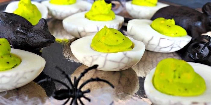 deviled eggs with green filling black dye halloween finger foods arranged on plattes with plastic spiders animals