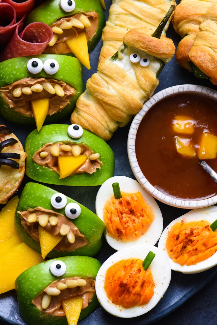 easy halloween appetizers peppers wrapped in dough as mummies salsa dip deviled eggs apples with peanut butter arranged on black paltter