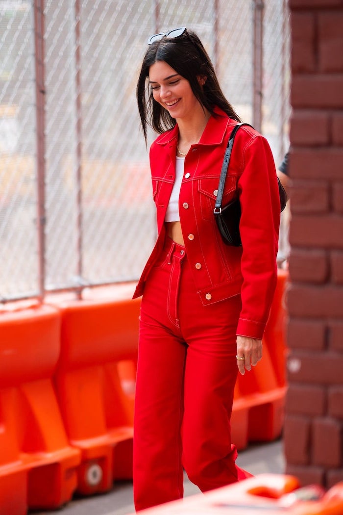 fall fashion trends kendall jenner photographed on the sidewalk wearing red jeans red denim jacket white crop top small black leather bag