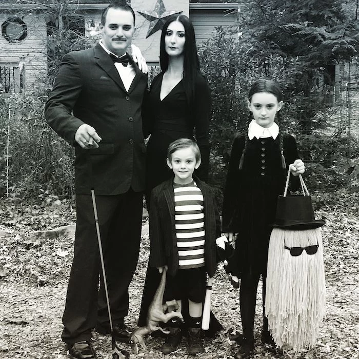 family of 3 halloween costumes family dressed as the addams family posing in old yard black and white photo