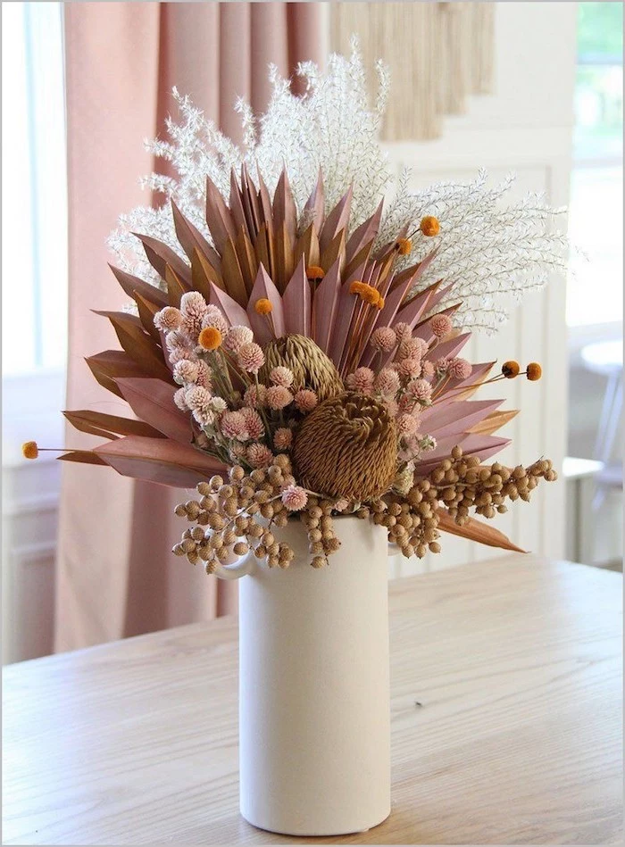 faux flowers arrangement in white pink gold dried pampas grass placed inside white ceramic vase placed on wooden table