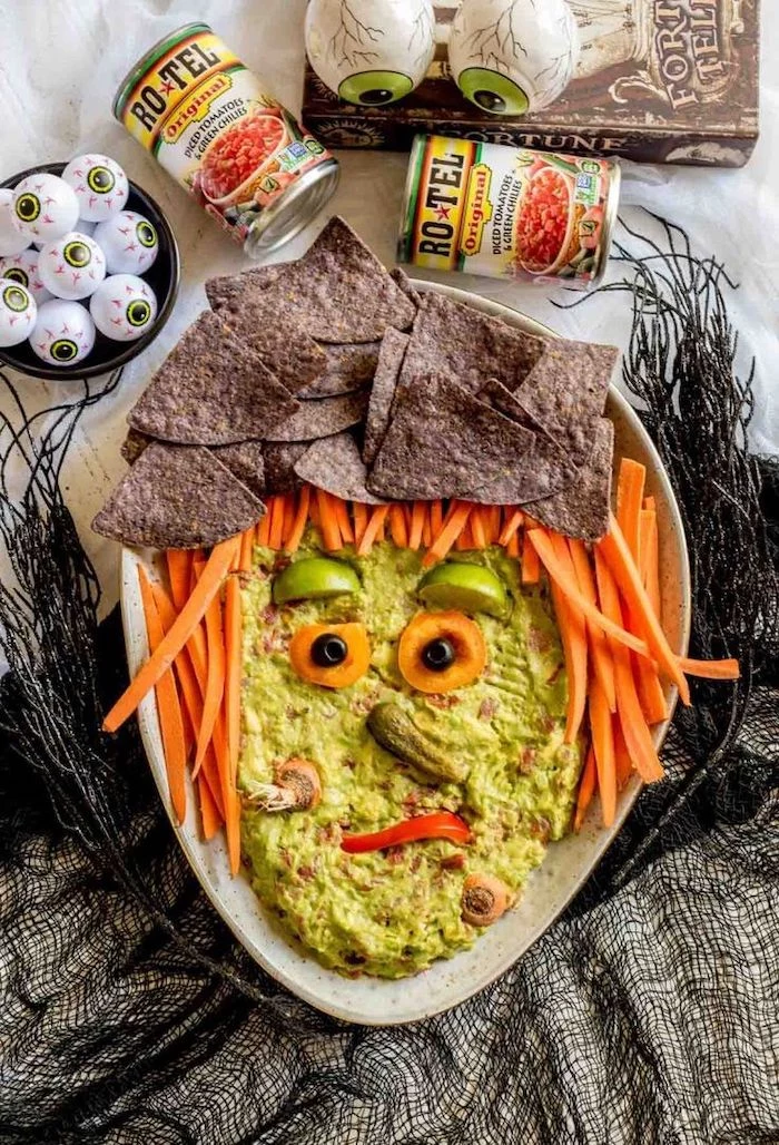 guacamole dip with baby carrots black tortilla chips halloween party food for adults arranged as with face on white platter