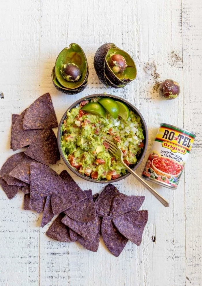 guacamole dip with tomatoes inside bowl black tortilla chips arranged on white wooden surface halloween party food for adults