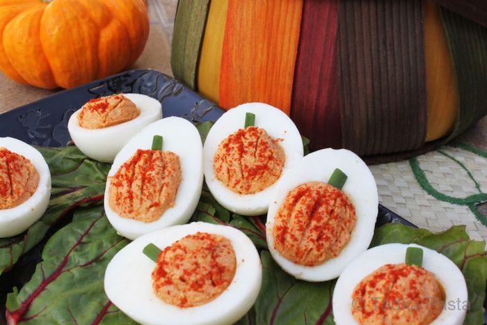halloween appetizer ideas deviled eggs with filling in the shape of pumpkin arranged on green leaves on blue tray