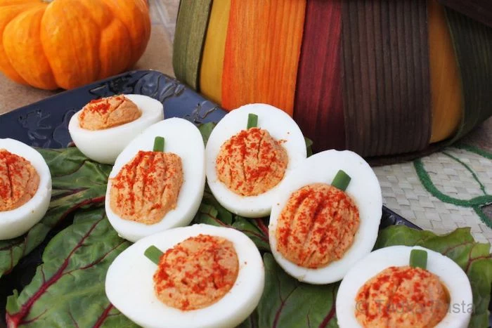 halloween appetizer ideas deviled eggs with filling in the shape of pumpkin arranged on green leaves on blue tray