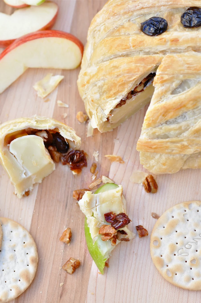 halloween party snacks baked brie with jam and walnuts baked as mummy with raisins for eyes placed on wooden surface