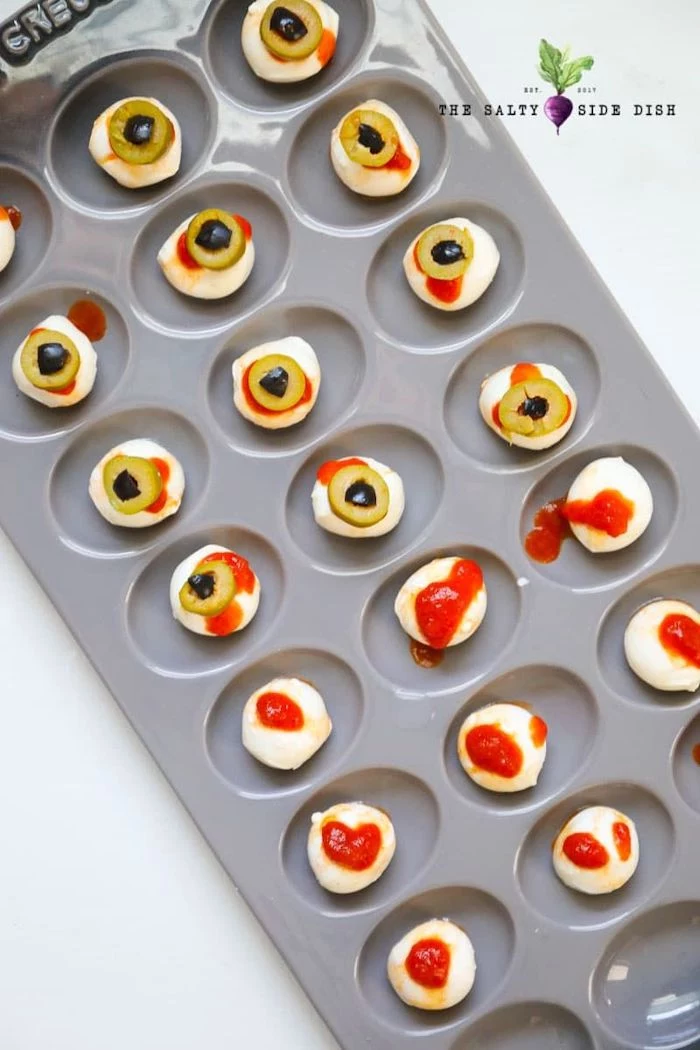 halloween party treats baby mozzarella with salsa and olives arranged in muffin baking tray placed on white surface