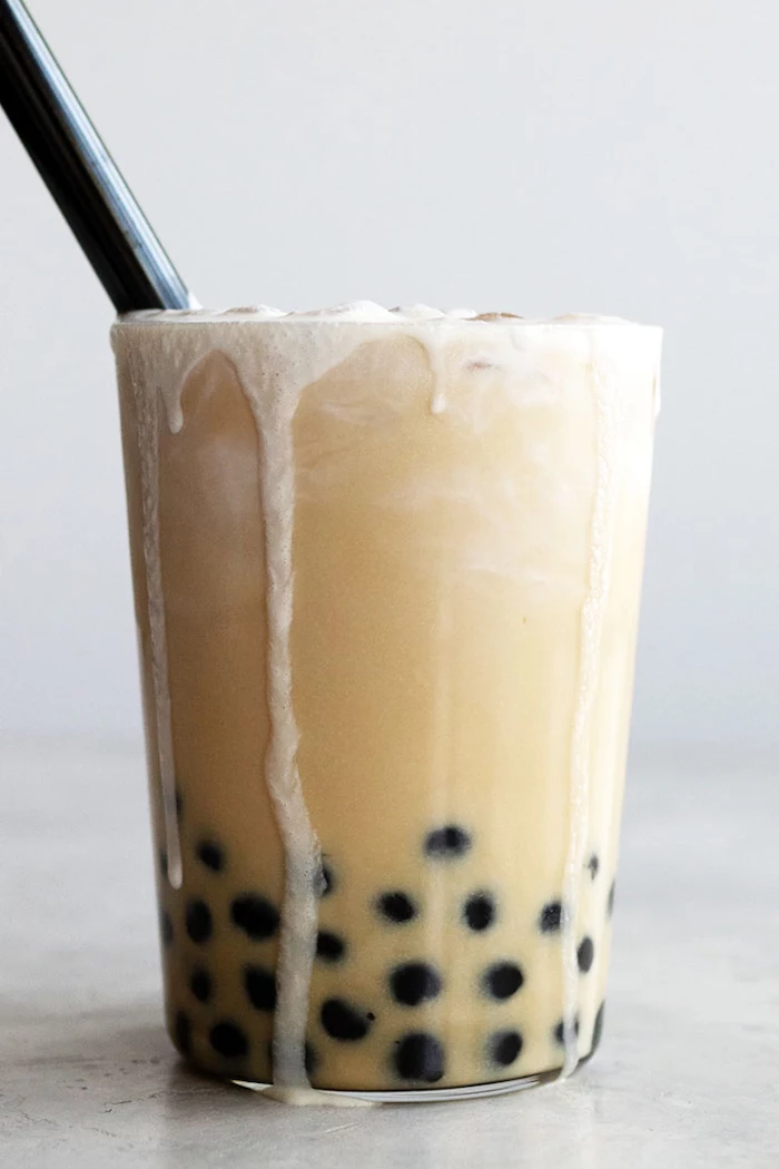 how to make bubble tea glass full of boba tea spilling out of the glass with ice and plastic straw on white background
