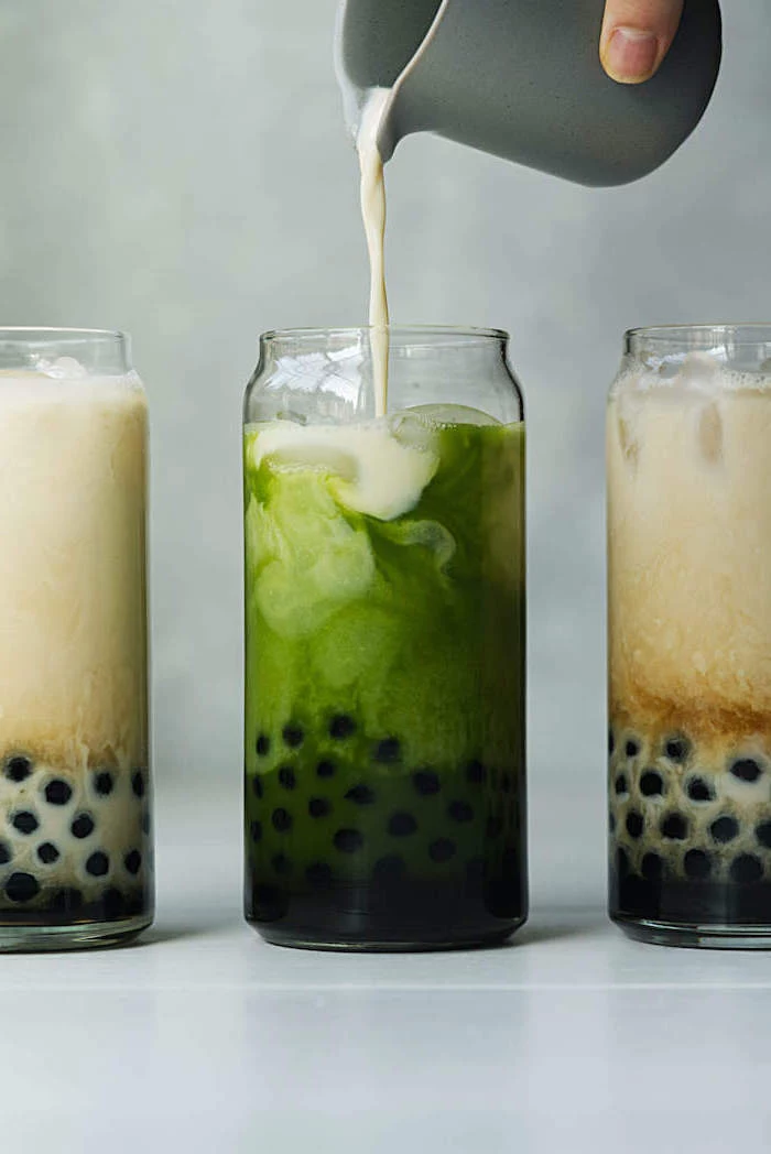 how to make milk tea milk being poured into tall glass filled with green bubble tea two more glasses next to it