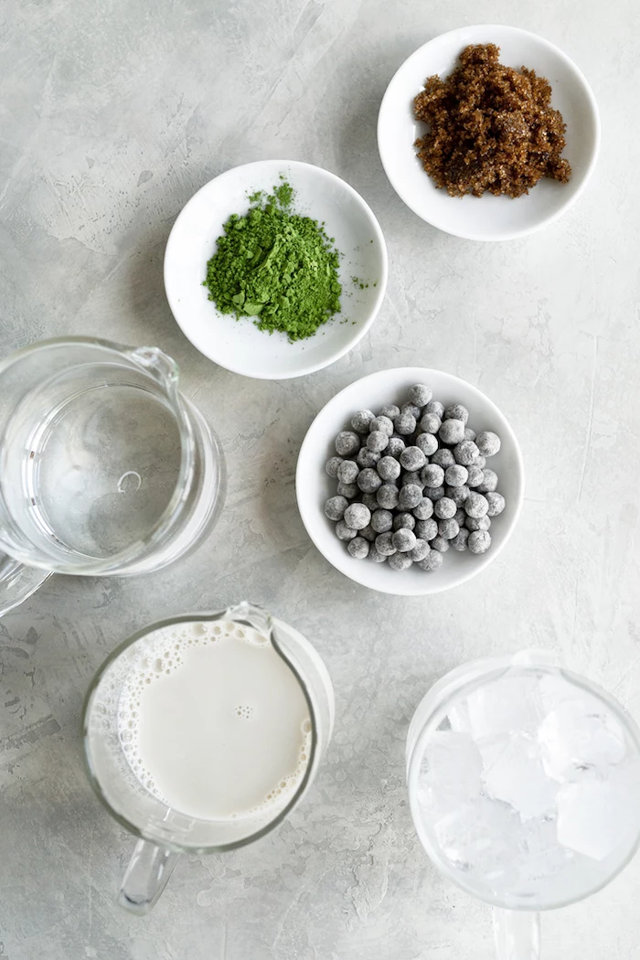 ingredients necessary for bubble tea recipe placed in white bowls and glass jugs arranged on white surface