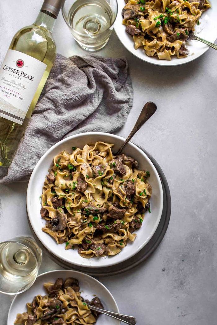 instant pot one pot meals beef stroganoff placed in white plates on granite surface glasses and bottle of wine on the side