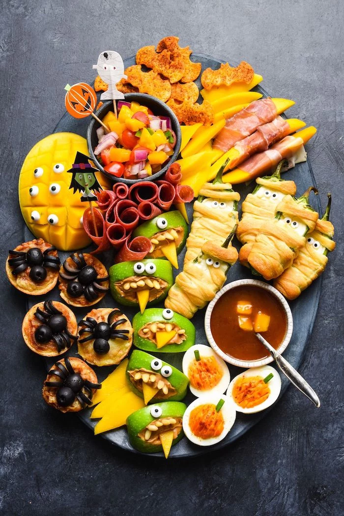 large black patter placed on gray surface halloween party treats crackers apples peppers cheese deviled eggs mango arranged on platter