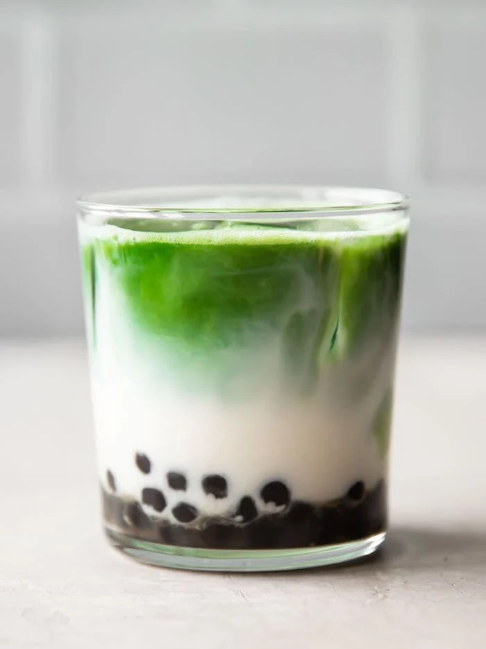 matcha bubble tea in glass filled with ice tapioca pealrs on the bottom placed on white surface how to make boba tea
