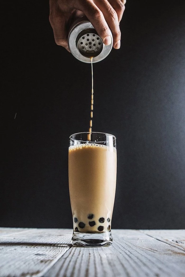 milk being poured into tall glass placed on wooden surface what is boba made of black background