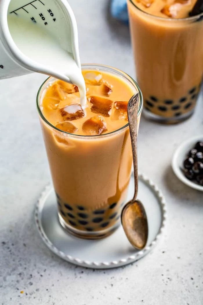 milk being poured into tall glass with bubble tea filled with ice what is boba teaspoon on the side