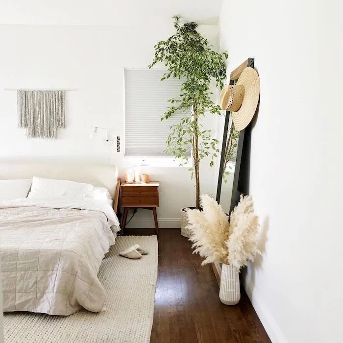 mirror leaning on white wall in bedroom with wooden floor tall pampas grass inside white ceramic vase