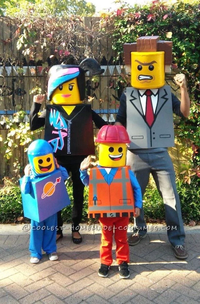 mom dad two kids dressed as lego people family halloween costume ideas standing in front of wooden wall and flower beds