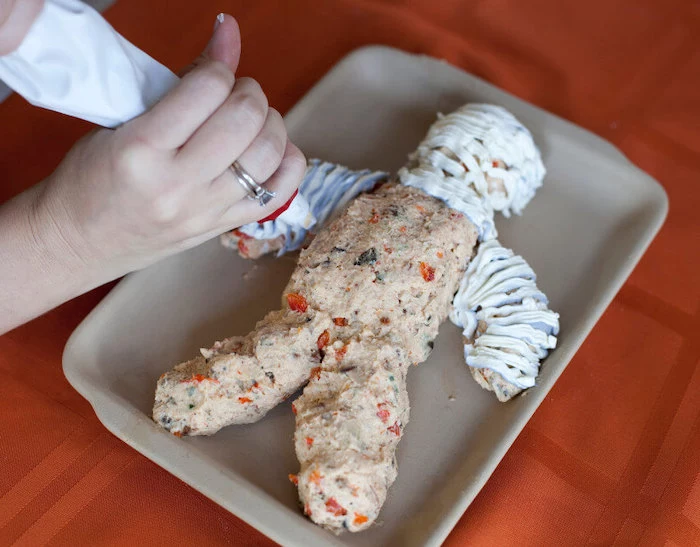 mummy made of cheese veggies halloween party snacks covered with cream cheese placed on gray baking tray
