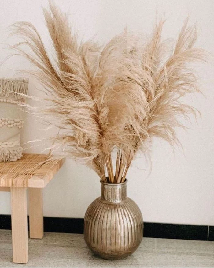pampas grass metal round vase with the plant inside placed on tiled floor next to small wooden bench