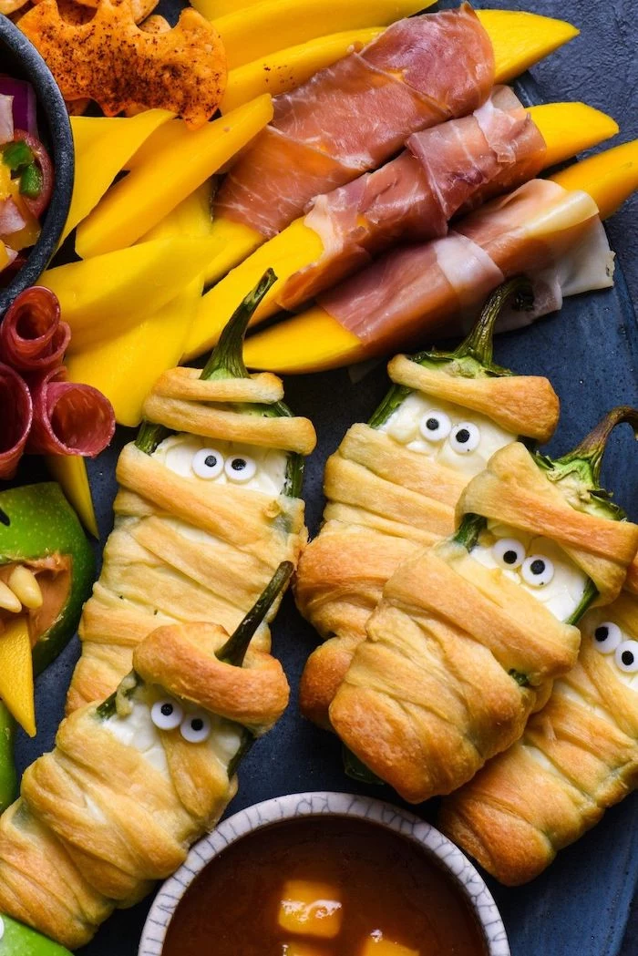 peppers wrapped with dough as mummies easy halloween appetizers cheese wrapped in prosciutto salami dip arranged on black platter