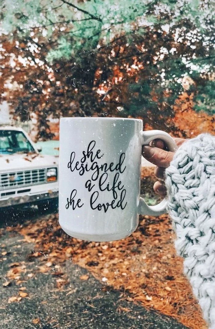 she designed a life she loved written on white mug cute fall backgrounds held by woman fall leaves in the background