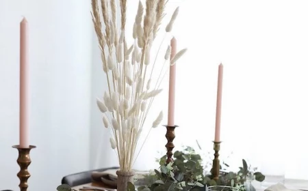 tall pampas grass in the middle of white table runner on wooden table three candles greenery on it