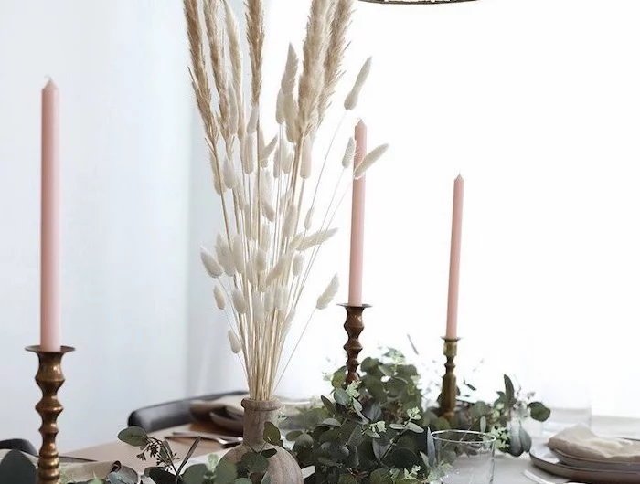 tall pampas grass in the middle of white table runner on wooden table three candles greenery on it