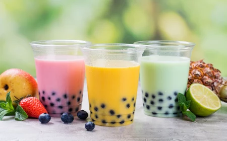 three plastic cups filled with pink yellow green bubble tea fruits scattered around them what is boba