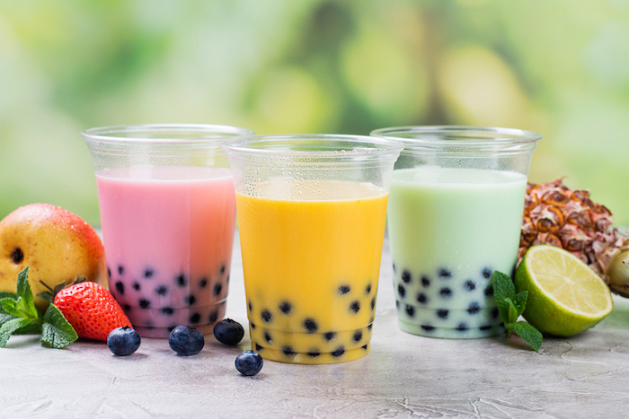 three plastic cups filled with pink yellow green bubble tea fruits scattered around them what is boba