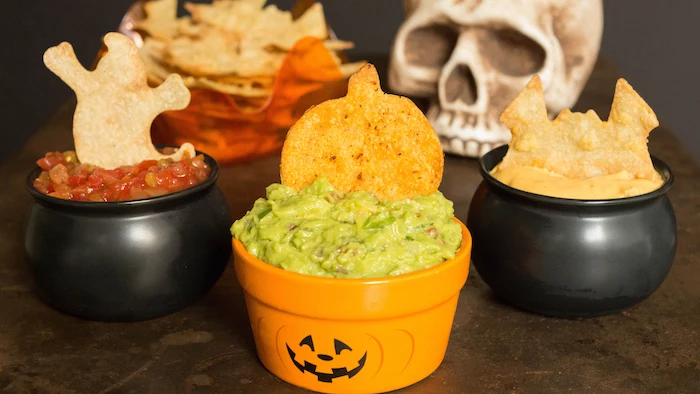 three small bowls in black and orange with different dips inside tortilla chips on top halloween snack ideas salsa guacamole