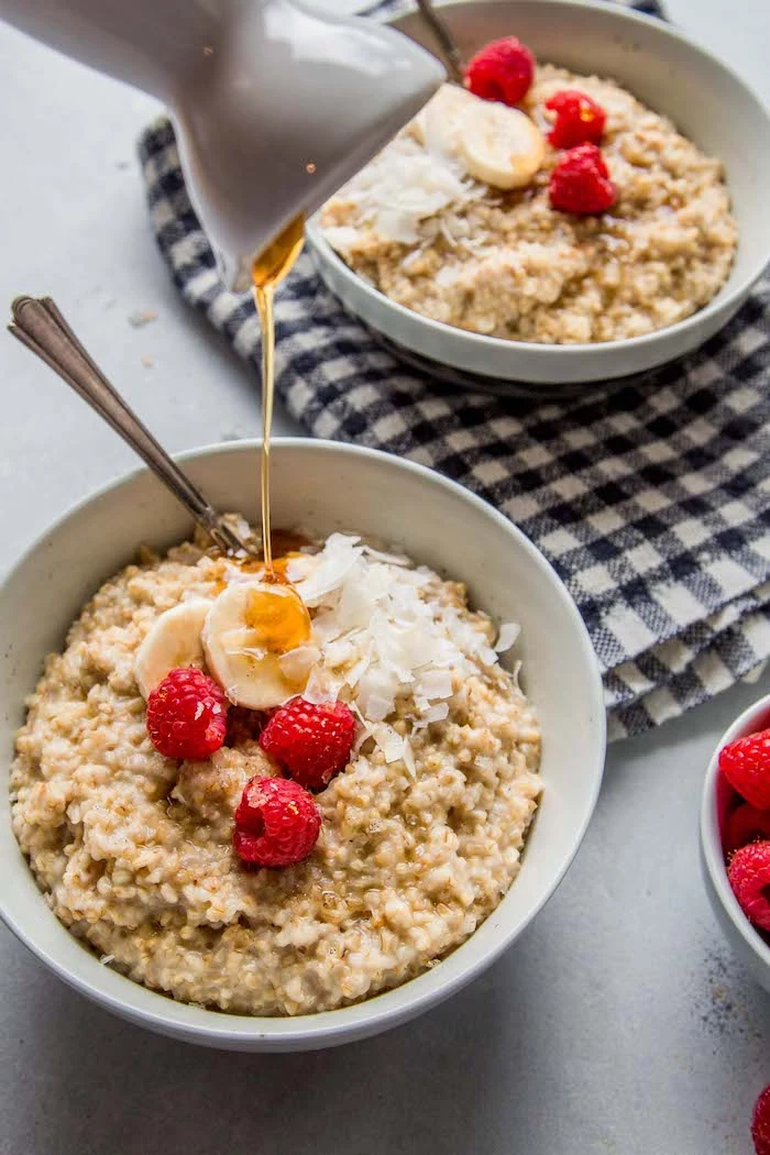 two white bowls filled with oatmeal with bananas raspberries shredded coconut healthy pressure cooker recipes honey poured over