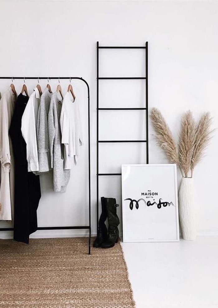 white walls behind black metal railing with coats hanging on it dried pampas grass inside white tall vase