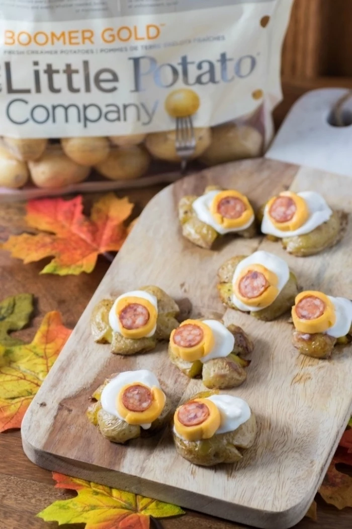 wooden cutting board on wooden table halloween appetizer ideas monster eye balls made with potatoes cheese sausages arranged on top