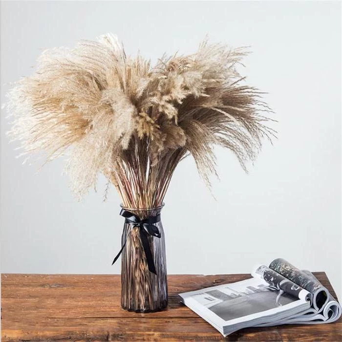 wooden table with open magazines on it glass vase with artificial pampas grass black bow tied around it