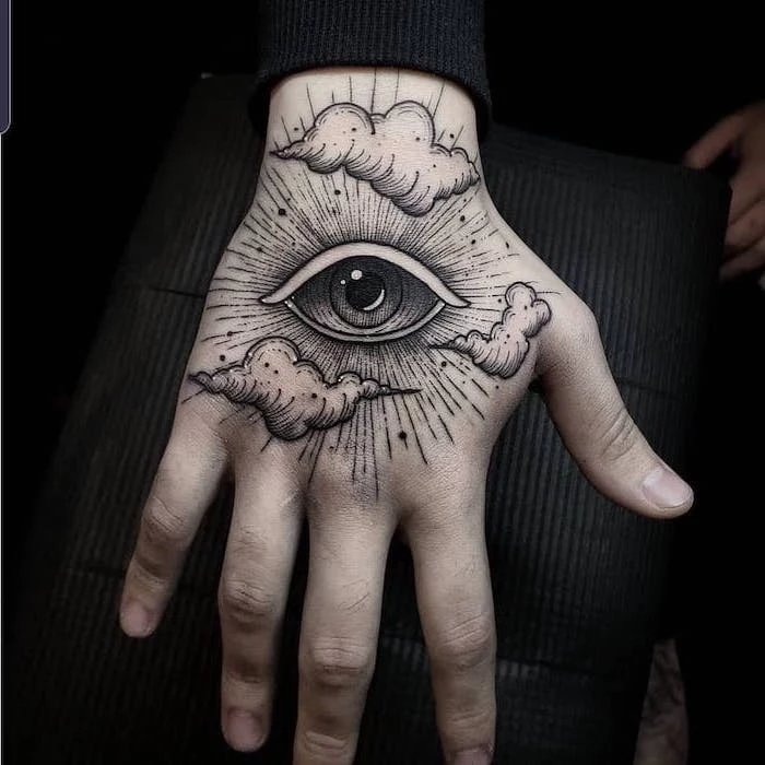 all seeing eye with clouds hand tattoo on man wearing black blouse tattoos with meaning of life black background