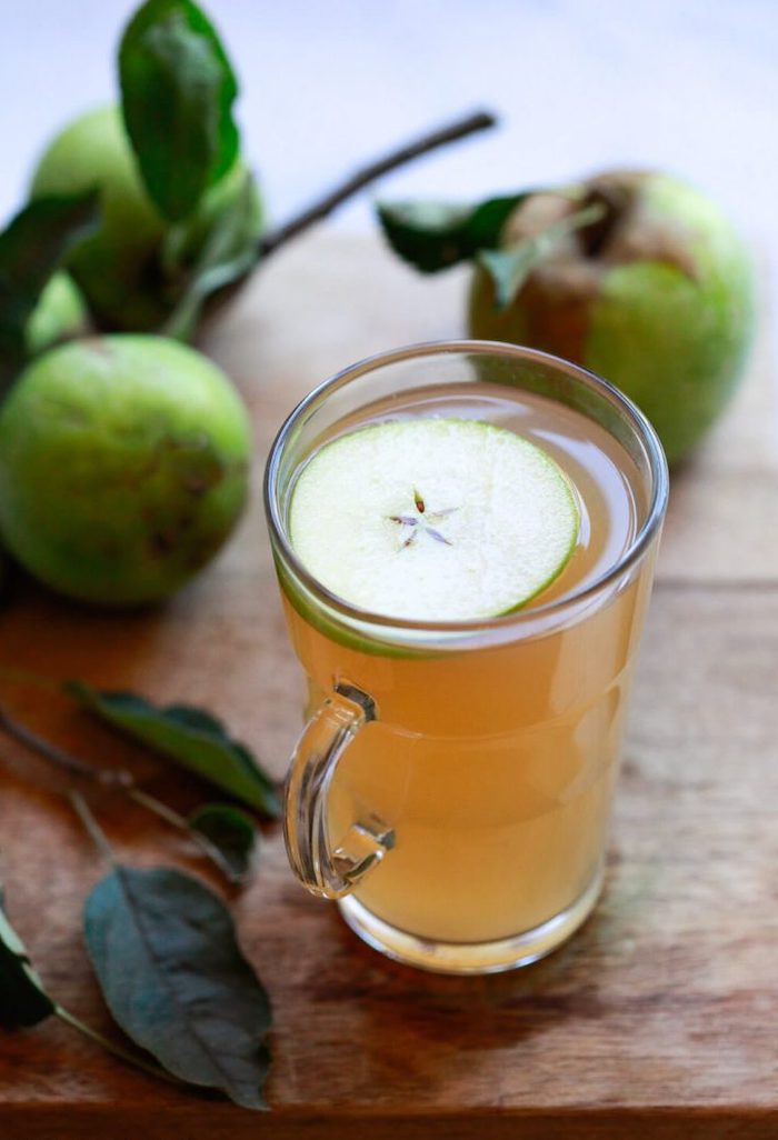 apple cider vinegar garnished with apple slice best detox cleanse for weight loss placed on wooden surface apples in the background