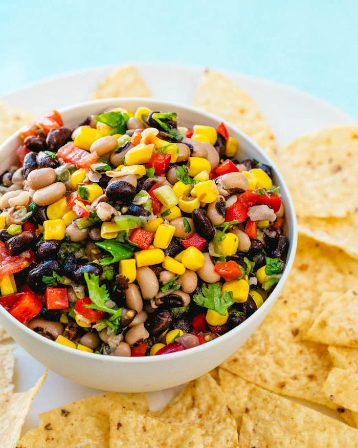 baked beans with corn peppers tomatoes chopped parsley in white bowl vegan party food tortilla chips around the bowl
