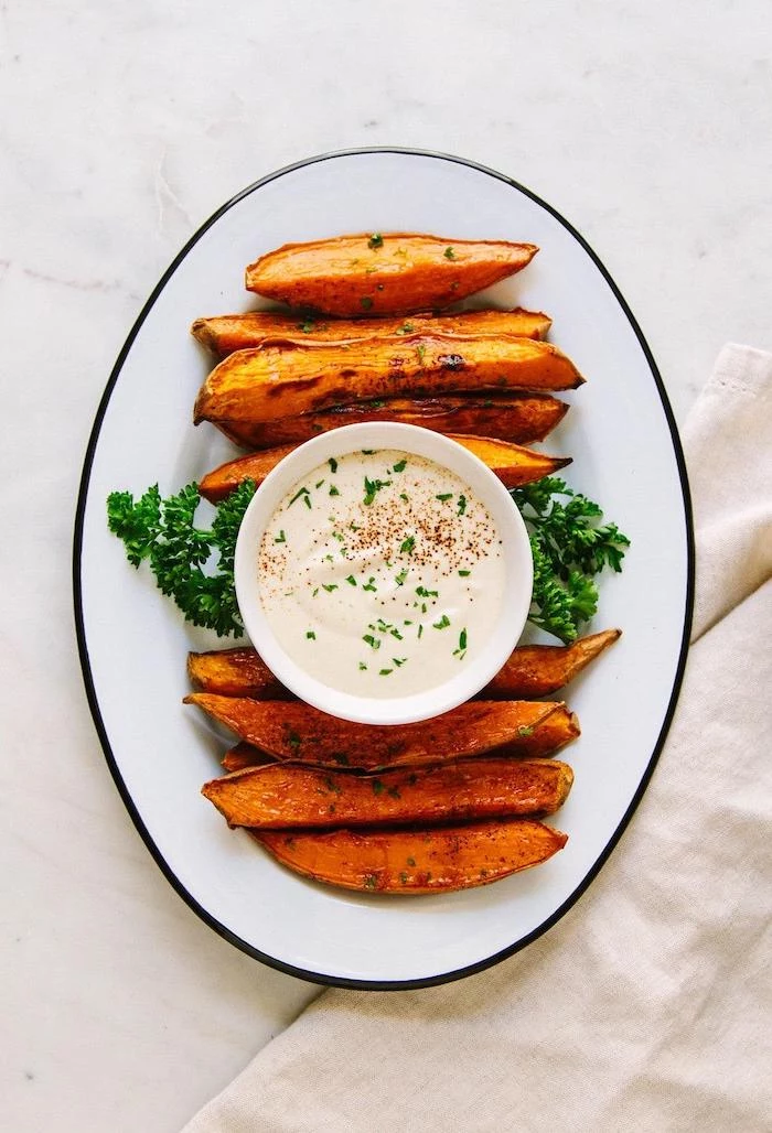 baked sweet potato wedges arranged on white plate best vegan appetizers small bowl in the middle with dip inside