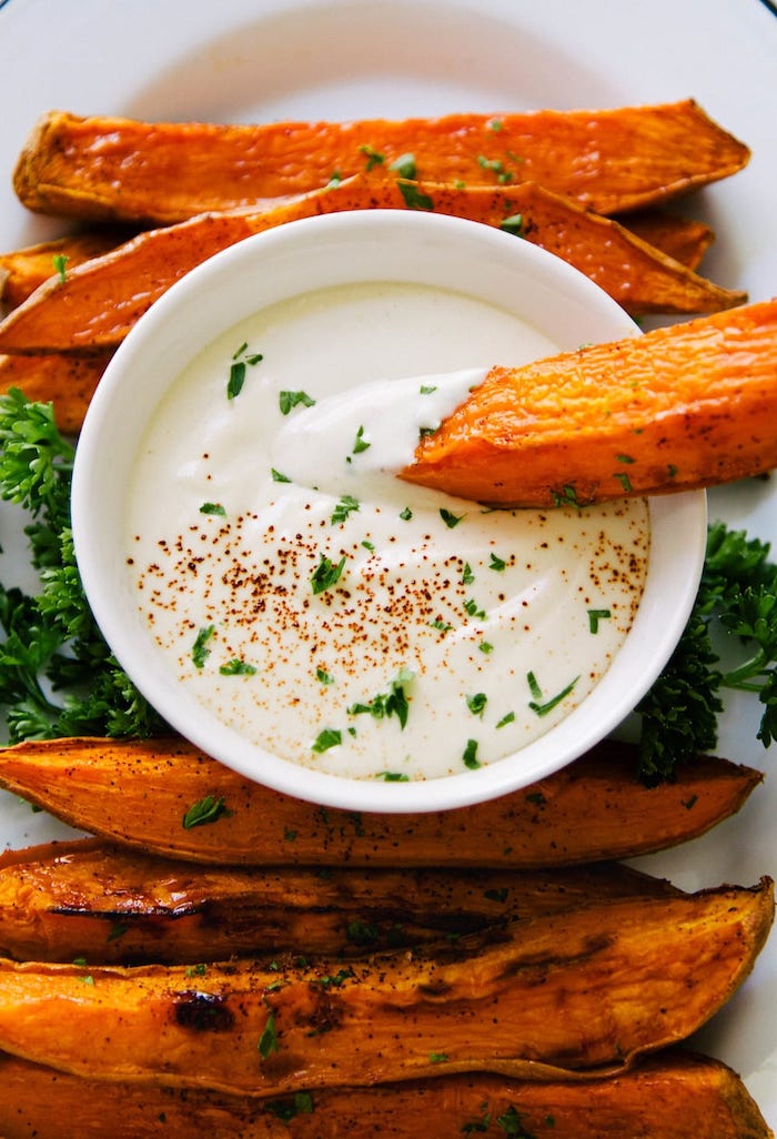 baked sweet potato wedges arranged on white plate vegan party appetizers dipped in white sauce in small white bowl