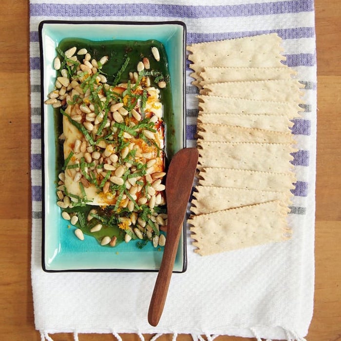 baked vegan cheese with pine nuts garnished with basil vegan appetizer recipes inside blue plate crackers on the side