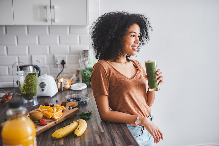 bananas oranges kiwi blueberries strawberries on wooden cutting board how to detox your body woman standing drinking green smoothie