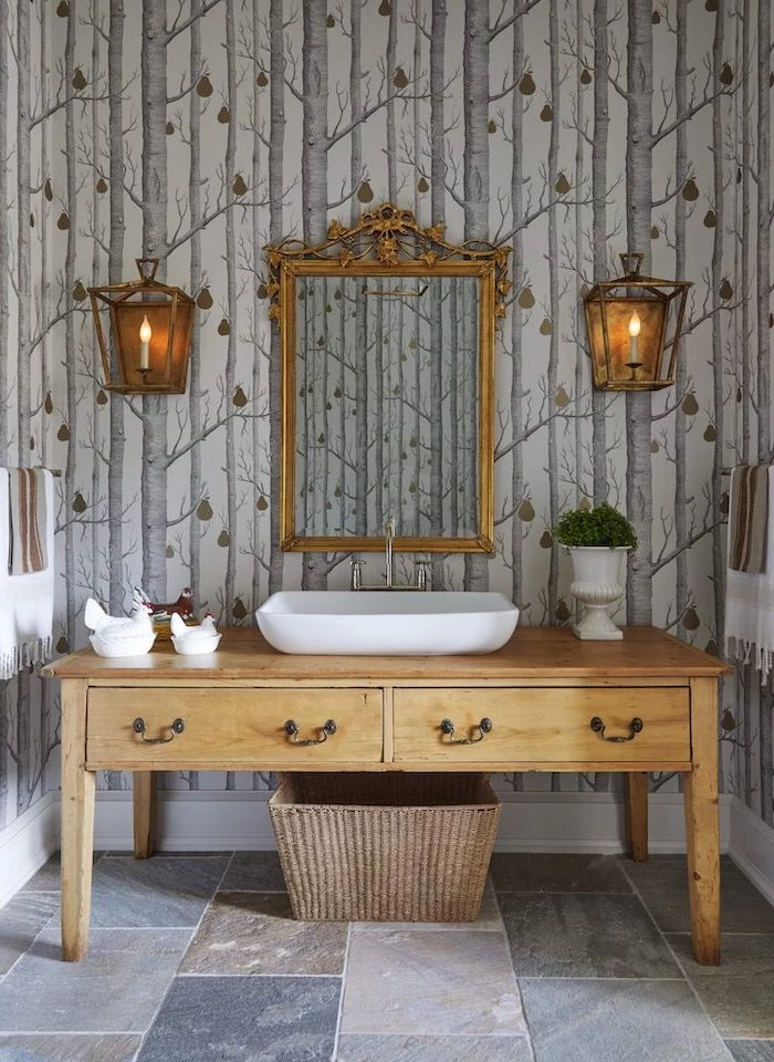 bathroom wooden vanity with sink mirror above it hanging on a wall with wallpaper with trees bathroom decor signs vintage lamps on both sides of the mirror