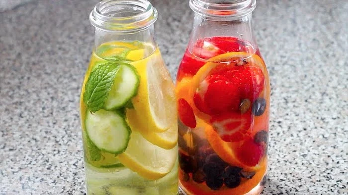 best detox cleanse two glass bottles one filled with cucumbers lemons and mint leaves other lemons strawberries blueberries