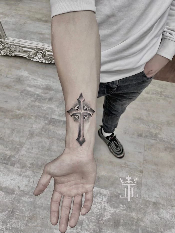 black and white cross tattooed on the wrist of man wearing jeans white blouse tattoos that represent growth