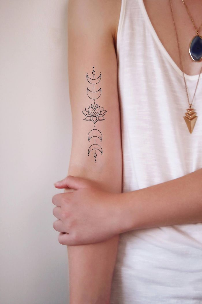 black and white small lotus with four moons around it strength symbol tattoo inside the arm tattoo on woman wearing white top