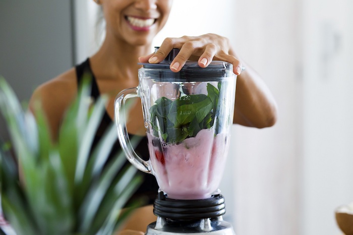 blender filled with ingredients for smoothie best detox cleanse lid held by woman wearing sports bra